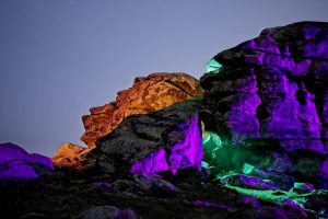 Rocks illuminated with green, purple, and orange lights against a twilight sky.
