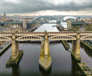 Aerial view of multiple bridges spanning over a river in a cityscape with overcast skies, highlighting urban architecture and infrastructure.