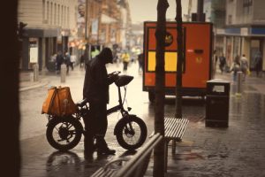 Street photography of a person with a bike on a rainy day, taken with an 85mm lens, capturing urban life and wet pavement reflections.