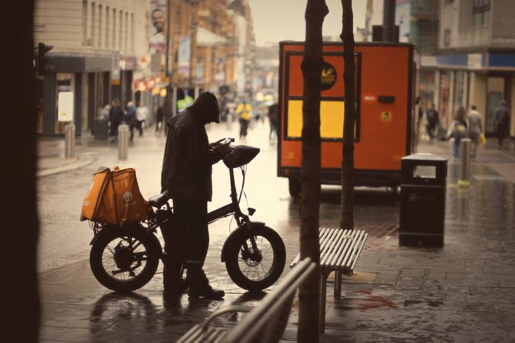 Street photography of a person with a bike on a rainy day, taken with an 85mm lens, capturing urban life and wet pavement reflections.