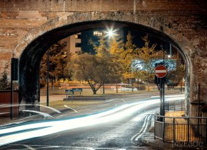 Long exposure of Leeds cityscape at night, with light trails under a brick archway.